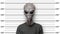 Police-style mugshot of an extraterrestrial being with grey skin and big eyes wearing t-shirt against height measurement ruler in