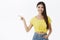 Polite and friendly charming european female model with long dark hair in trendy yellow cropped t-shirt pointing left