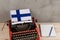 Political news and education concept - red typewriter, flag of the Finland, notebook on gray cement background