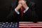 The politician-businessman clasped his hands thoughtfully as he sat at a table covered with an American flag, thinking