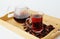 Pomegranate flowers tea in glass cup closeup. Teapot in the background. Bamboo tray with scattered petals. Ruby infusion