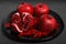 Pomegranate fruit and red mini pepper laid out on a black plate, on a neutral gray background