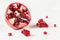 Pomegranate halved, few gem like fruits clusters scattered on white working board next to it