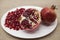 Pomegranates have broken into pieces with red berries on a porcelain plate on a textile background.