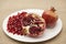 Pomegranates have broken into pieces with red berries on a porcelain plate on a textile background.