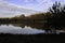 Pond in autumn with sunrise over background of frozen water, trees in November colors with blue sky and cloud