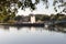 Pond with a bridge and a fountain on the island. The foliage of the tree hangs over the lake.