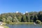 Pond with green trees on the shore. The towers of the building in the blue sky, peeking from the trees.