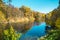 A pond with yellow and green trees on steep banks with a beautiful reflection of the blue sky in the water on a clear sunny day. N