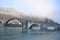 Ponte della Maddalena built in stone under a cushion of fog, called the devil`s bridge, illuminated on the left by the sun of a co