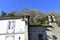 Ponte Maceira, Coruna, Spain. Wall with sundial, iron light and Camino de Santiago symbol. San Blas chapel bell tower with trees a