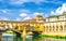 Ponte Vecchio bridge with colourful buildings houses over Arno River blue reflecting water historical centre of Florence