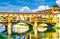 Ponte Vecchio stone bridge with colourful buildings houses over Arno River blue reflecting water in historical centre of Florence