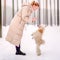 A poodle stands on its hind legs in front of a woman attentively listens to her commands