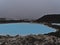 Pool with blue thermal water between lava rocks with steaming Svartsengi power station in background near Blue Lagoon, Iceland.