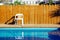 Pool side suburban villa back yard space without people here white plastic chair and wooden wall background with lights and