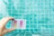Pool tester test kit in girl hand with space on blurred clear swimming pool water background