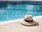 Poolside still life. Straw hat on floor next to resort swimming pool. Glittering crystal clear blue water in sunlight.