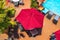 Poolside textured red umbrellas over tables and chairs beside lounges covered in beach towels and potted palms on orange tile deck