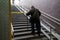 poor adult man leans on a cane and climbs the stairs from the underpass