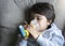 Poor boy tired from chest coughing holding inhaler mask, Child closing his eyes while using the volumtic for breathing treatment,