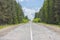 A poorly-paved rural two-lane road, deciduous forest, cloudy sky, highway to the horizon