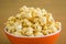 Popcorn in orange bowl. Brown background