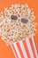 Popcorn pouring from a paper bowl to a orange background, and 3d glasses for watching the movie, a top view