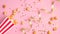 Popcorn in red and white paper bucket scattered on pink background with golden ribbon and confetti