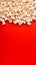 Popcorn scattered on a red background. A classic movie theater snack. View from above