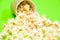 Popcorn spills out of a brown paper cup on a green background close-up