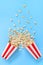 Popcorn spills out of the paper striped cups on a blue background. A splash of popcorn. Vertical view