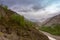 Poplar trees and small running river small lying in a rocky valley underlying blue cloudy sky