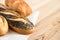 Poppy seed baguette and bread rolls lying on white burlap on light wood. Space for text