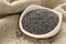 Poppy seeds in white ceramic bowl on sackcloth background