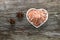 A porcelain bowl in the shape of a heart filled with large crystals of pink himalayan salt on an old weathered board, next to it