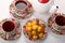 Porcelain teacups with hot tea and with floral pattern, teapot, biscuits and plate with wild apricots on a white tablecloth