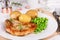 Pork chop, boiled jacket potatoes and green peas served on a plate