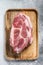 Pork neck piece on brown wooden chopping board. Gray background. Top view