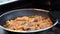 Pork in the pan is being deep fried in boiling oil, being stirred by a spatula.