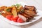 Pork ribs, potatoes and tomatoes on a plate close-up