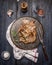 Pork roast on an iron skillet with a napkin, fork, sauce, salt and pepper on rustic wooden background