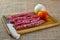 Pork sausage. thin pork sausage on wooden cutting board with knife, tomato and onion next to it on jute fabric