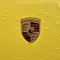 Porsche logo closeup, yellow sports car, rain drops