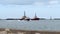 PORT ARANSAS, TX - 14 FEB 2020: The EMMA KATE boat sails past two tug boats and the South Jetty as a dolphin surfaces in the water