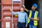 Port manager and a colleague tracking inventory while standing point to position loading Containers box from Cargo freight ship