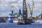 A port tug is towing a floating crane in the port of St. Petersburg. Nuclear icebreakers under construction in the background