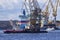 A port tug is towing a floating crane in the port of St. Petersburg. Nuclear icebreakers under construction in the background