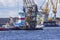 A port tug is towing a floating crane in the port of St. Petersburg. Nuclear icebreakers under construction in the background