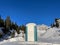 Portable chemical toilet in idyllic snow-covered winter landscape.